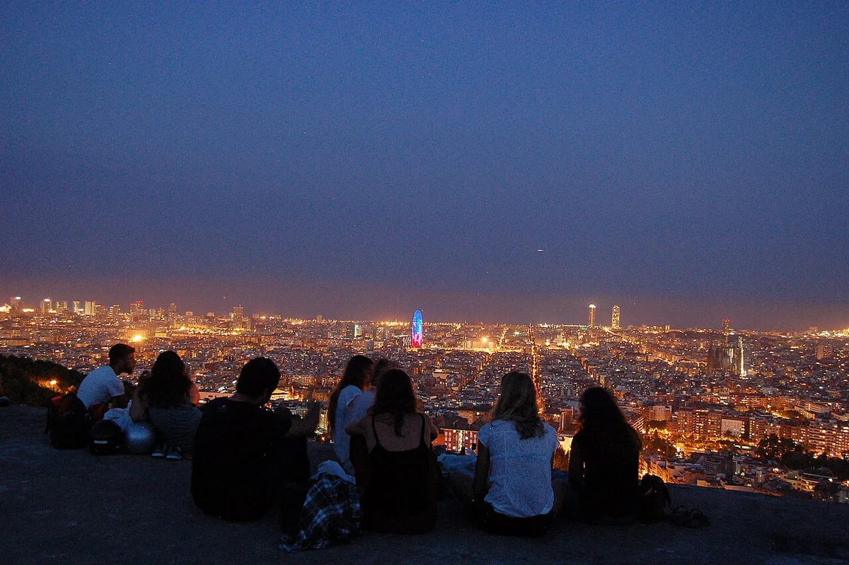 Bezoekers genieten bij nacht van het panoramische uitzicht over Barcelona vanuit de Turó de la Rovira, het hoogste uitkijkpunt van het Parc del Guinardó